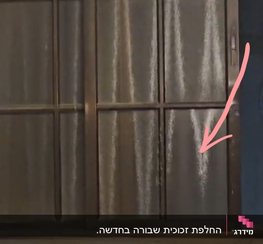 חלון אלומיניום עם זכוכית פגומה המסומנת בחץ אדום לפני תיקון